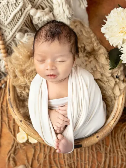 A classic newborn pose, swaddled snugly in a basket with a neutral, earthy theme. This style is timeless and keeps the focus on the baby's peaceful state.