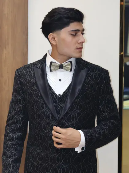 The full view of the black textured tuxedo, showing the satin lapels and the way the fabric catches the light. A perfect choice for a wedding reception.