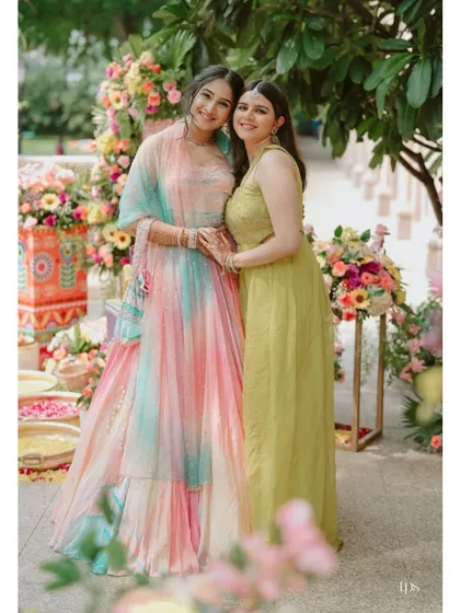 The bride, in her stunning multi-colored lehenga, shares a happy moment with a guest at her Haldi ceremony.