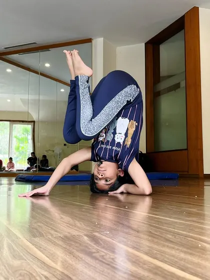 The body achieves what the mind believes. This young gymnast holds a creative leg variation in her headstand, exploring her balance and flexibility.