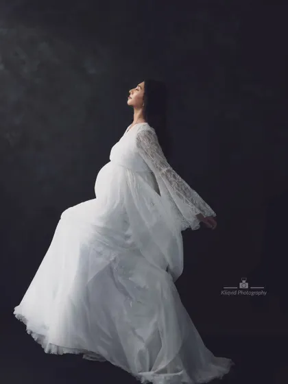 Embrace the beauty of this magical time. This ethereal portrait in a flowing white lace gown celebrates the joy of motherhood.