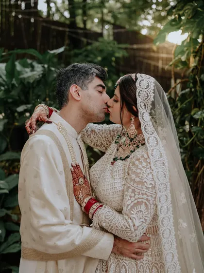 A kiss of celebration. This golden hour shot captures the couple sharing a kiss, the sun flaring perfectly behind them, creating a warm, romantic, and dreamy atmosphere.