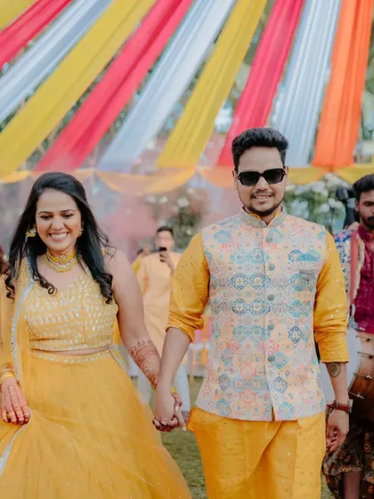 A happy couple walks hand-in-hand under the colourful drapes of their Haldi ceremony. The decor is designed to be bright and cheerful, reflecting the celebratory mood of the event.