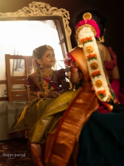 A girl in traditional attire looks at her reflection in a mirror, her hair beautifully decorated with 'moggina jade'. A behind-the-scenes style shot of a traditional look.