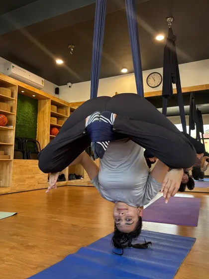 A student smiles while holding an inverted pose. The playful nature of aerial yoga makes even challenging asanas feel accessible and fun.