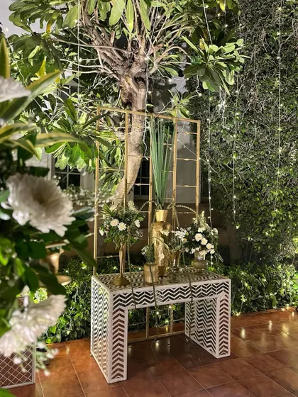 A beautiful floral setup in a corner, blending white blooms with gold accents and modern geometric consoles, all against a backdrop of fairy lights.