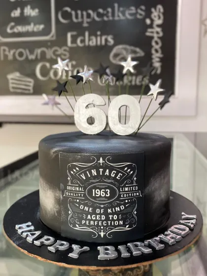 A stylish and masculine cake for a 60th birthday. The black cake features a "Vintage 1963, Aged to Perfection" edible label, silver lettering, and a spray of stars on top.
