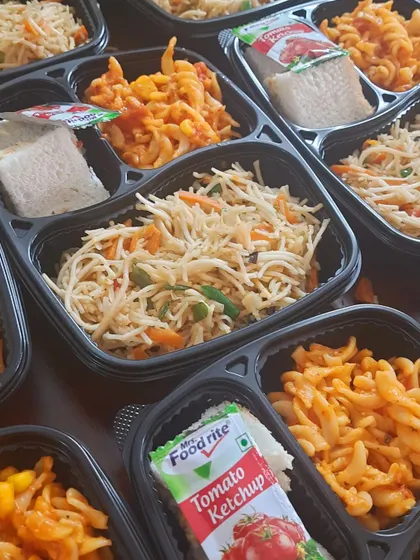 Our party boxes offer great variety. Here you can see a mix of veg hakka noodles, red sauce pasta, and sandwiches, ready to be distributed at an event. It's a simple solution for feeding a crowd.