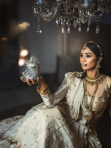 A regal portrait of a bride in an elegant white and gold ensemble. The lighting, pose, and luxurious setting all contribute to a sophisticated and timeless bridal photograph.