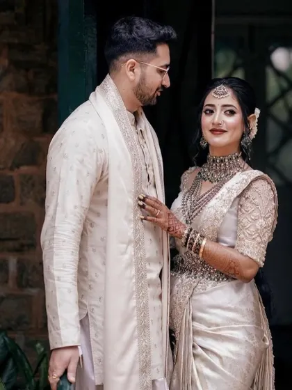 The groom looks lovingly at his bride, dressed in a custom off-white sherwani. The clean lines and subtle embroidery make it a sophisticated choice for a modern wedding ceremony or engagement.