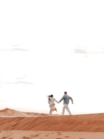 A sense of adventure and freedom as the couple runs hand-in-hand over the crest of a sand dune. This dynamic shot captures the joy of their shared journey.