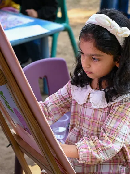 A young girl concentrates on her painting at an easel during the Mela. We foster creativity by providing artistic activities for children at our events.