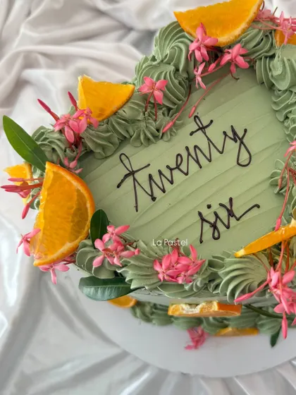 A top-down view of the heart-shaped sage green cake, showing the beautiful arrangement of oranges and flowers.