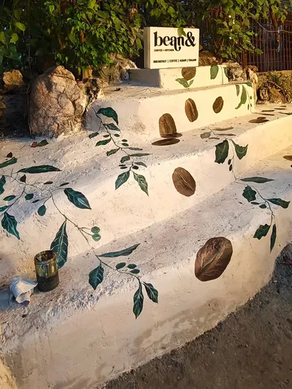 Art can extend beyond walls to any surface. For 'bean&' cafe, I painted their branding elements, including coffee beans and leaves, directly onto the outdoor concrete steps, creating a unique and welcoming entrance.