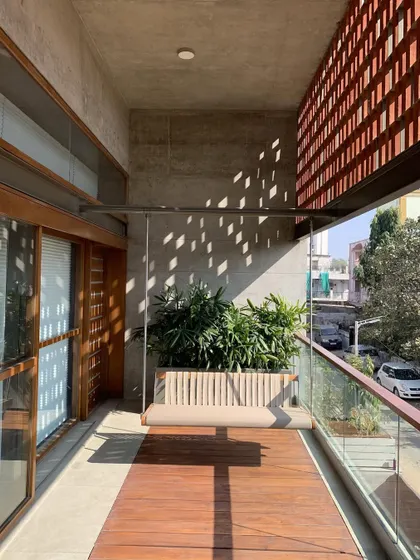 This balcony design combines a wooden deck with a built-in planter and a hanging swing. The terracotta jali screen adds privacy and a traditional touch to the modern setup.