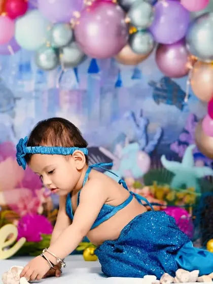Exploring her underwater kingdom. This wide shot shows the complete mermaid setup with a balloon arch, a castle backdrop, and seashells.