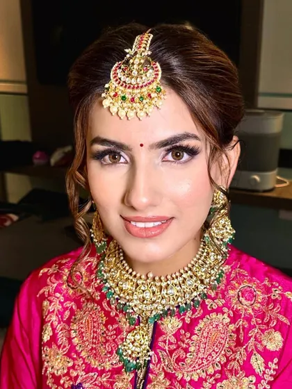 A beautiful Punjabi bride. The look features a classic winged liner, a bright bindi, and a natural lip color, all designed to complement her vibrant pink suit and traditional jewelry.