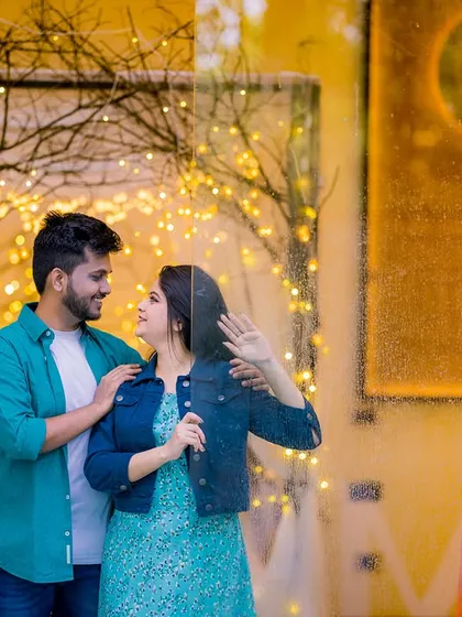 A romantic moment behind a glass door, with fairy lights creating a magical glow. The couple's casual outfits make this shot feel intimate and real.