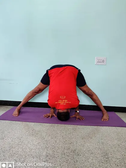 Prasarita Padottanasana with the head on the floor and hands between the feet, showing a deeper stage of the forward bend.