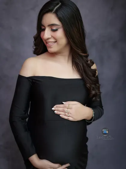 A fitted black gown can create a stunningly elegant and modern maternity portrait. This off the shoulder, mermaid style dress beautifully accentuates her form, while her gentle smile adds a touch of warmth.