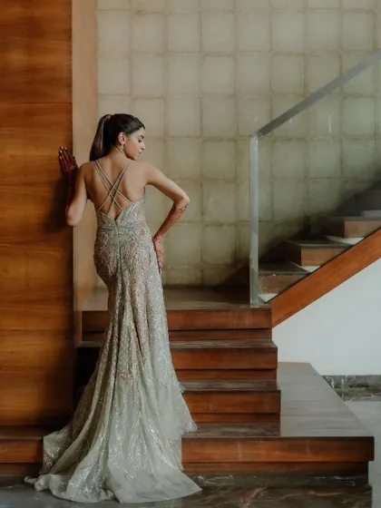 A stylish and modern bridal portrait. The backless design of her shimmering gown and the clean lines of the wooden staircase create a sophisticated and contemporary image.