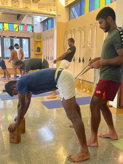 Using a belt to provide traction and resistance in Adho Mukha Svanasana (Downward-Facing Dog). This helps the athlete to lengthen the spine and open the shoulders more effectively.