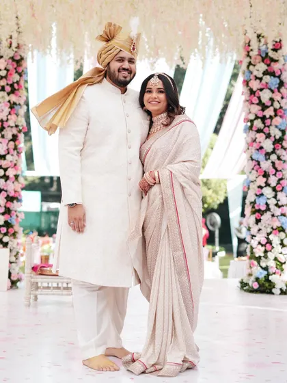 A full-length portrait showcasing the couple's elegant white and red outfits against a backdrop of stunning floral pillars. The composition is grand and celebratory.