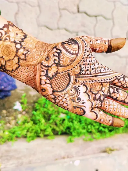 A beautiful, stained party mehendi design photographed in natural greenery. The design is a mix of floral and paisley motifs.