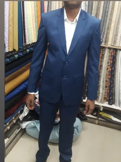 A client fitted for a classic two-piece suit in navy blue. The background shows the variety of suit fabrics available in my shop.