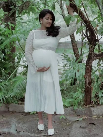 A classic pose for a solo maternity shoot. The mother holds a branch, connecting with the nature around her, while cradling her baby bump.