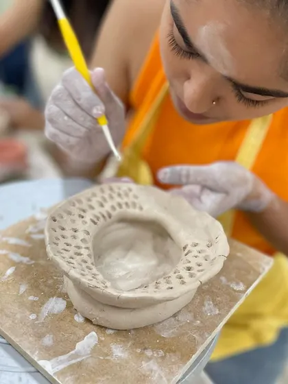 A student carefully pierces a pattern into the edge of their hand-built piece, a technique that requires patience and a steady hand.
