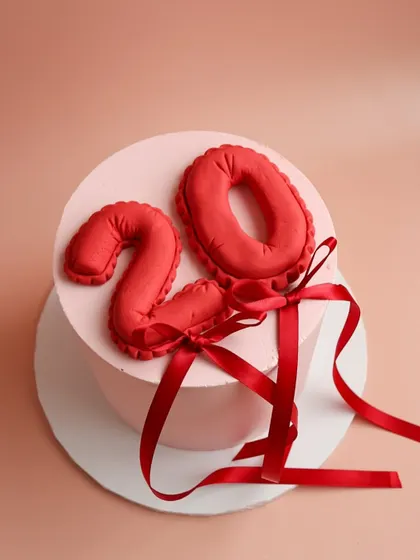 A minimalist and pretty 20th birthday cake with a red fondant balloon number and matching ribbon.