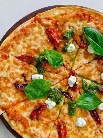 A delicious pizza topped with sun-dried tomatoes, fresh basil, pesto, and creamy goat cheese.