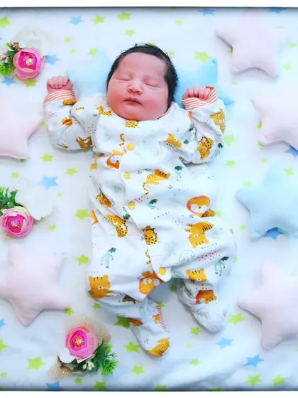 Twinkle, twinkle, little star. This peaceful newborn is sleeping on a star-patterned blanket, surrounded by soft star pillows and floral accents.