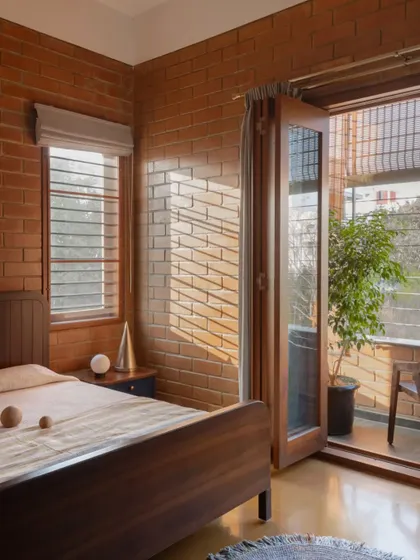 Sunlight streams into this bedroom, highlighting the texture of the exposed brick and warming the wooden furniture. A small balcony offers a private connection to the outdoors.