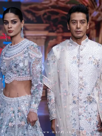 A close-up of the off-white couple's ensemble on the runway. The groom's sherwani features delicate floral multicolor embellishments, a showcase of timeless elegance.