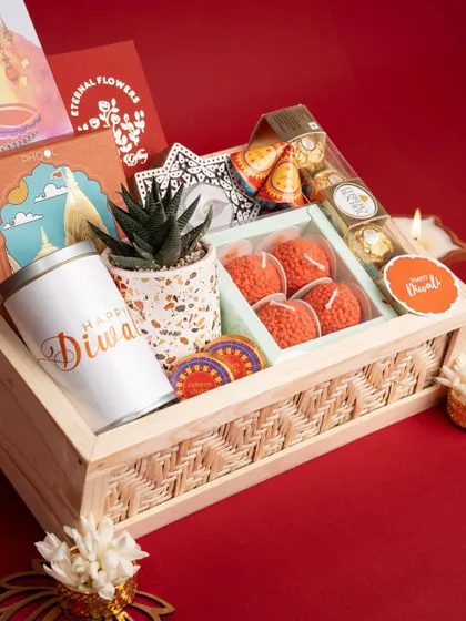 A luxury Diwali hamper, featuring a custom 'Happy Diwali' tin, motichoor laddoo-shaped candles, Ferrero Rocher, and a succulent plant in a festive pot.