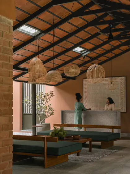 The reception and seating area features custom-built wooden furniture with clean lines and dark green upholstery. Skylights in the tiled roof ensure the space is filled with natural light throughout the day.