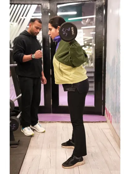 A trainer provides support and guidance as a client performs a barbell squat, a fundamental movement for building overall strength.
