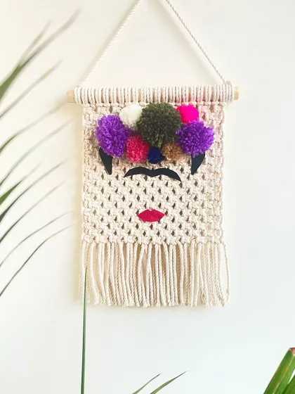 My tribute to the iconic artist, Frida Kahlo. This wall hanging captures her signature look with a floral crown made of colorful pom-poms and bold red lips.