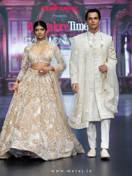 A full-length shot of the runway couple. The groom stands tall in a gold sherwani with geometric accents, a perfect blend of tradition and trend.