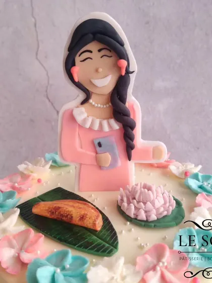 A cake celebrating all of Mansi's favorite things. This 1 kg Milk Chocolate Truffle cake is topped with a custom figurine and decorated with fondant versions of 'ela ada' and a lotus, surrounded by buttercream flowers.