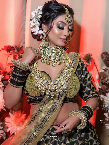 A graceful shot of the bride looking down, with warm red lighting in the background. The contrast in colors makes the gold of her lehenga and jewellery stand out even more.