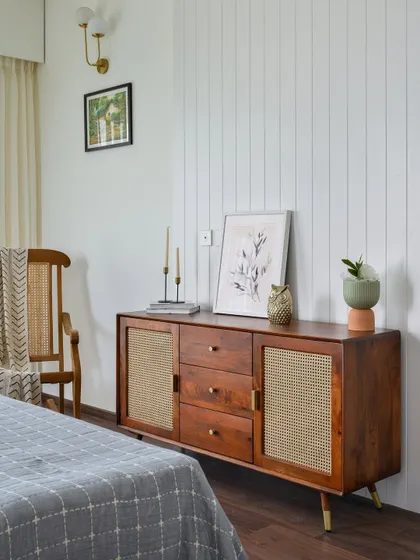 The master bedroom in 'Malhar' features a paneled wall that serves as a stylish backdrop and a future provision for a TV. The sleek sideboard with cane doors adds texture and warmth.