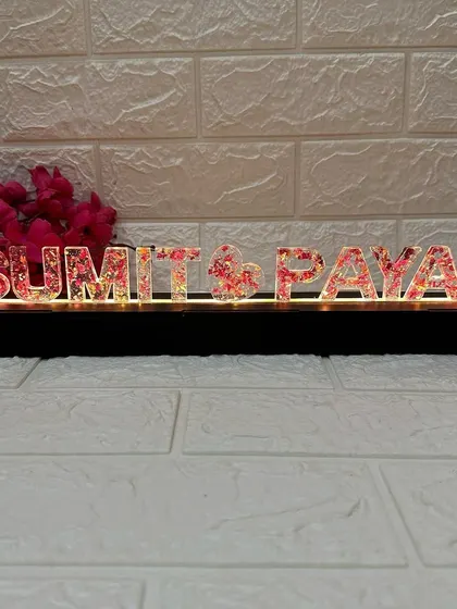 A full view of the "Sumit & Payal" LED name stand. It sits on a sleek black base that contains the lights, making it a perfect tabletop piece.