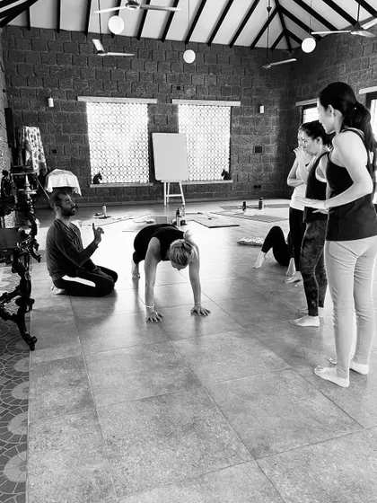 In our teacher training, students learn the art of observation and correction. Here, a teacher-in-training learns to guide a fellow student into a deeper, more aligned forward fold.