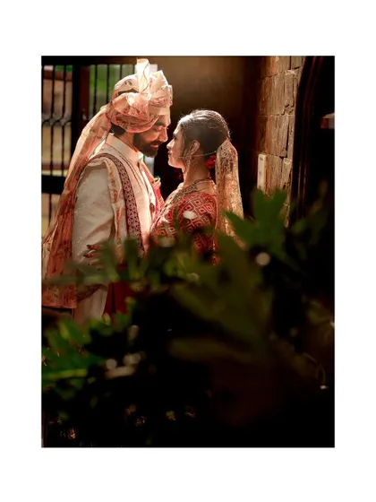 A beautifully framed shot of the bride and groom, their intimate moment partially obscured by greenery, adding a sense of privacy and romance.
