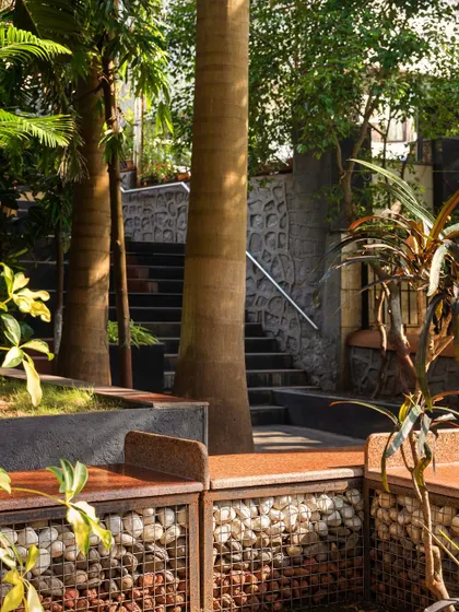 **Nepean Greens, Mumbai:** We used gabion walls filled with colored pebbles for the benches, topped with red Lakha stone. This material choice is durable, cost-effective, and adds a unique textural element that blends with the natural surroundings.