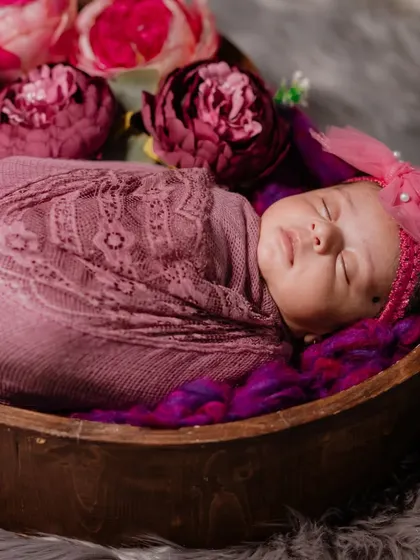 A beautiful newborn girl surrounded by deep pink peonies. The rich colors and textures create a warm and artistic portrait.