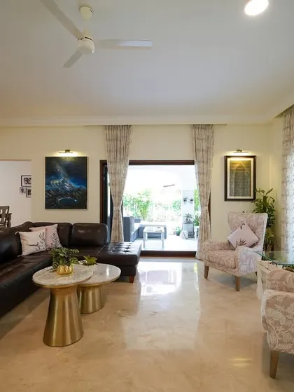 A closer view of the living space, where a dark leather sofa is balanced by patterned armchairs and delicate decor, creating a cozy yet refined atmosphere with a seamless indoor-outdoor connection.